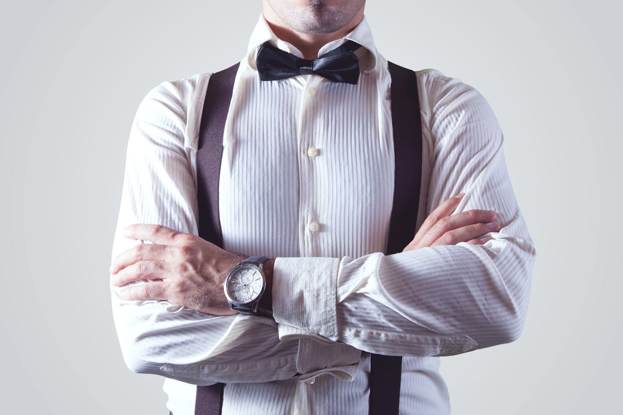A stylish man crossing his arms, dressed elegantly in a bow tie and suspenders.