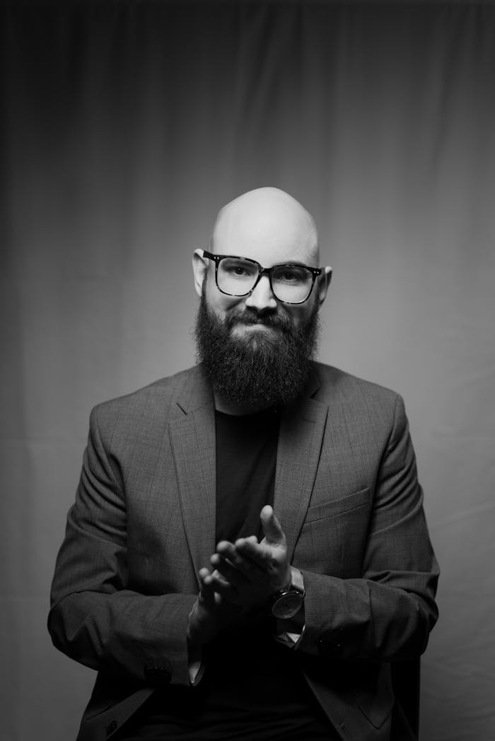 Monochrome portrait of a bearded man in a suit, clapping. Captures contemplative mood.