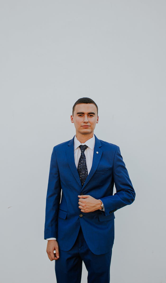 A confident man in a stylish blue suit poses against a plain background, exuding elegance and professionalism.