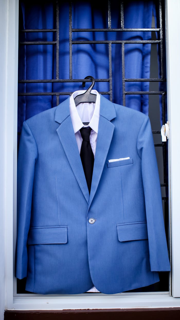 A stylish blue suit with tie displayed on a hanger against a windowpane.
